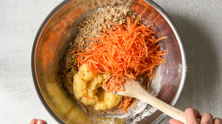 Adding shredded carrots, crushed pineapple, chopped walnuts, and golden raisins to vegan carrot cake batter