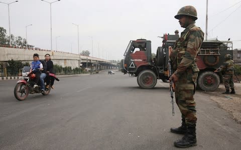 An Indian Army soldier stands guard as a family rides on a motorbike during a curfew in Jammu - Credit: Reuters