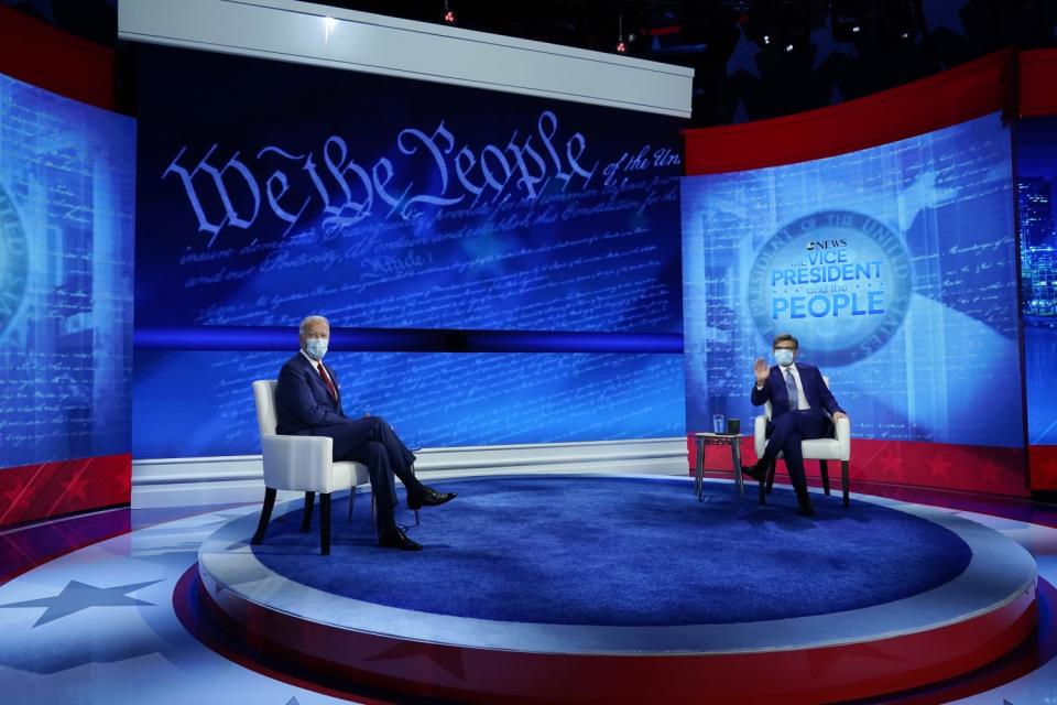 Joe Biden in a mask sits on a town hall stage across from ABC host George Stephanapoulos