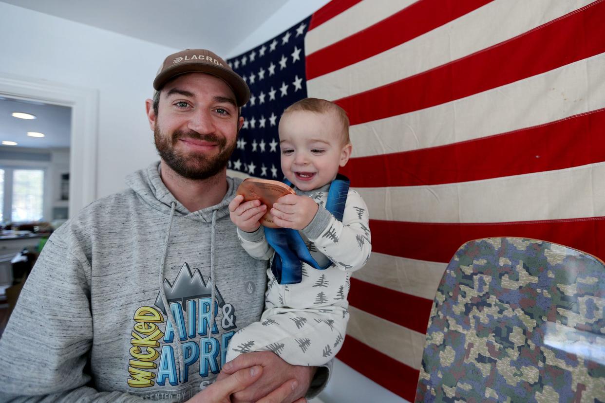 Scotty Lago holds his son, Ryder, who holds the bronze medal his father won at the 2010 Winter Olympics in their South Hampton home Monday, Jan. 31, 2022.