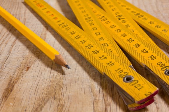 A long yellow measuring stick and yellow pencil side by side on a wooden table.