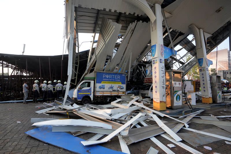 Members of rescue teams stand at a damaged fuel station after a massive billboard fell during a rainstorm in Mumbai