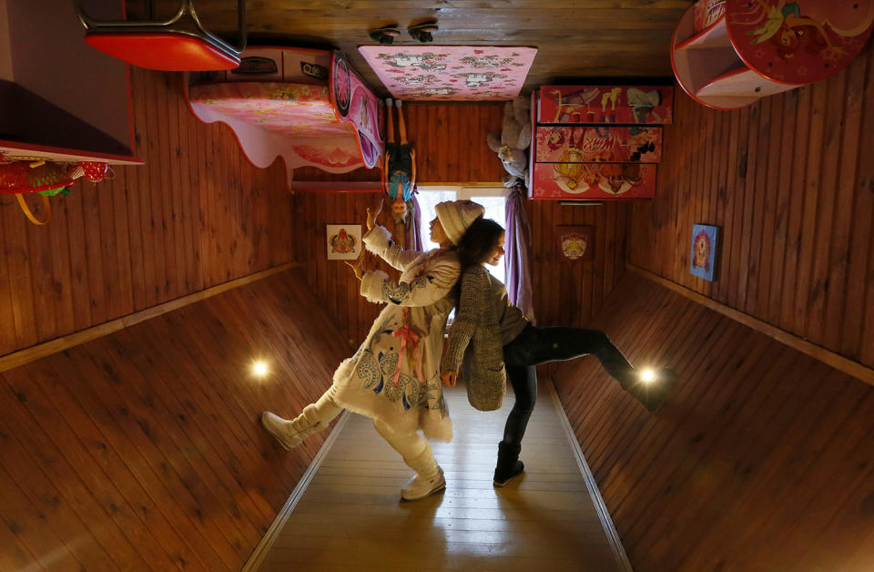 A visitor and an employee dressed as Snegurochka pose for a picture inside an upside down house