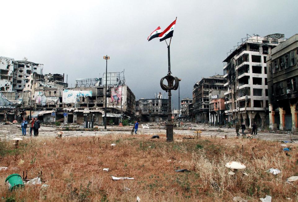 Two Syrian national flags hang on a pole as government officials inspect damages in the old city of Homs, Syria, Thursday, May 8, 2014. Hundreds of exhausted Syrian rebels withdrew Wednesday from their last remaining strongholds in the heart of Homs, surrendering to President Bashar Assad a bloodstained city that was once the center of the revolt against him. For Assad, it is a powerful victory ahead of presidential elections. For the rebels, the dramatic exit after two years of enduring grueling assaults and siege captures their sense of abandonment amid world reluctance to help shift the balance of power on the ground. (AP Photo)