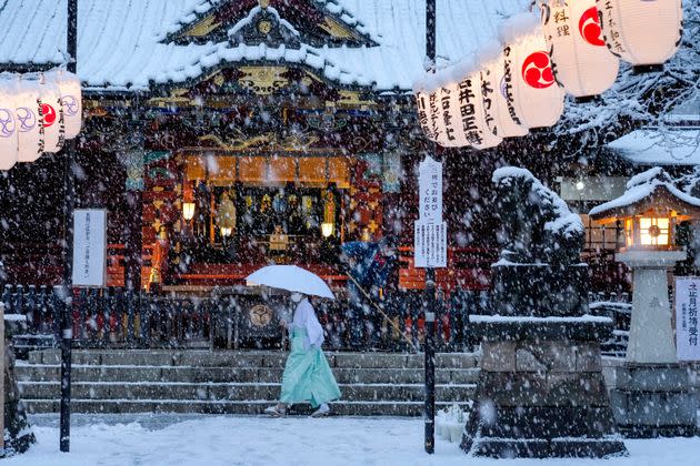 A shrine maiden walks past the main shrine while a worker clears the steps as snow falls down Thursday in Tokyo. (Photo: Kiichiro Sato/AP)