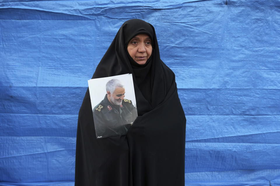 A woman holds a portrait of the late Revolutionary Guard Gen. Qassem Soleimani, who was killed in Iraq in a U.S. drone attack in 2020, during a funeral procession for a group of unknown Iranian soldiers who were killed during the 1980-88 Iran-Iraq war, whose remains were recently recovered in the battlefields, in Tehran, Iran, Tuesday, Dec. 27, 2022. (AP Photo/Vahid Salemi)