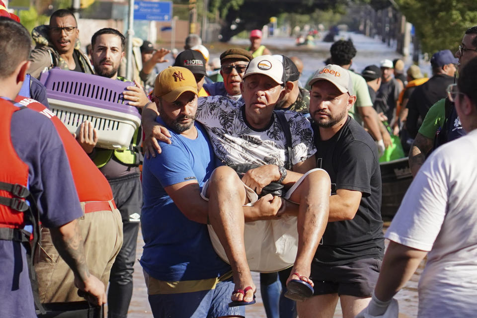 Volunteers carry an elderly man rescued from an area flooded by heavy rain in Porto Alegre, Rio Grande do Sul state, Brazil, Tuesday, May 7, 2024. (AP Photo/Carlos Macedo)