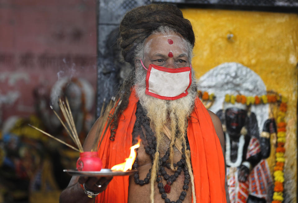 An Indian priest covers his face with a mask as a precaution against coronavirus and prays at a temple, in Prayagraj, India, Monday, June 8, 2020. Religious places, malls, hotels and restaurants open Monday after more than two months of lockdown as a precaution against coronavirus. (AP Photo/Rajesh Kumar Singh)