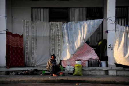 A woman sits and looks on outside a building covered up with sheets to protect the dwellers from the strong summer sun outside of the disused Hellenikon airport, where stranded refugees and migrants are temporarily accommodated in Athens, Greece, August 10, 2016. REUTERS/Michalis Karagiannis