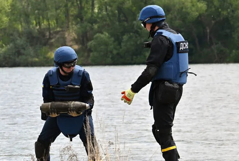 Los desminadores ucranianos recolectan material sin explotar durante los trabajos en Blue Lake, en el pueblo de Horenka, región de Kiev, el 27 de mayo de 2022. (Photo by Sergei SUPINSKY / AFP)