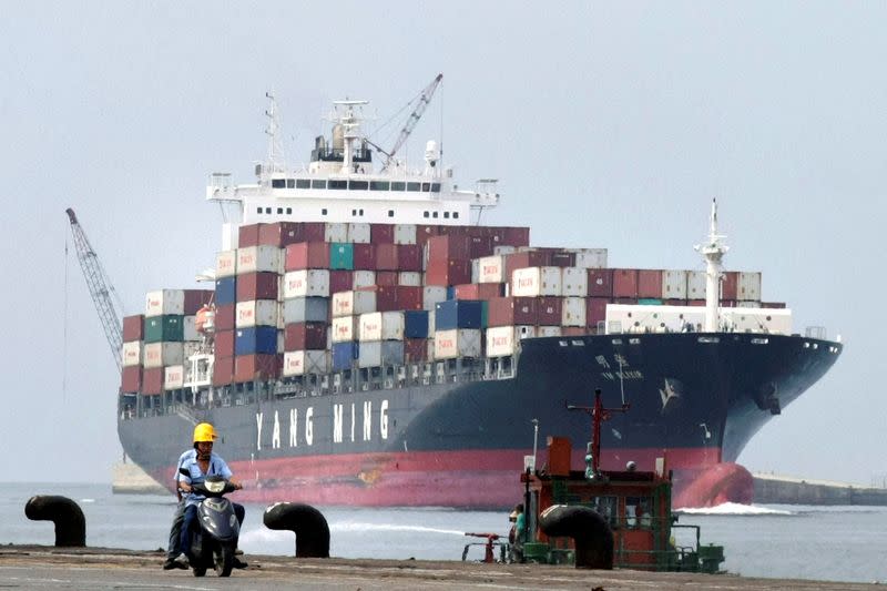 FILE PHOTO: People ride a motorcycle while a container ship passes by at Keelung port in northern Taiwan