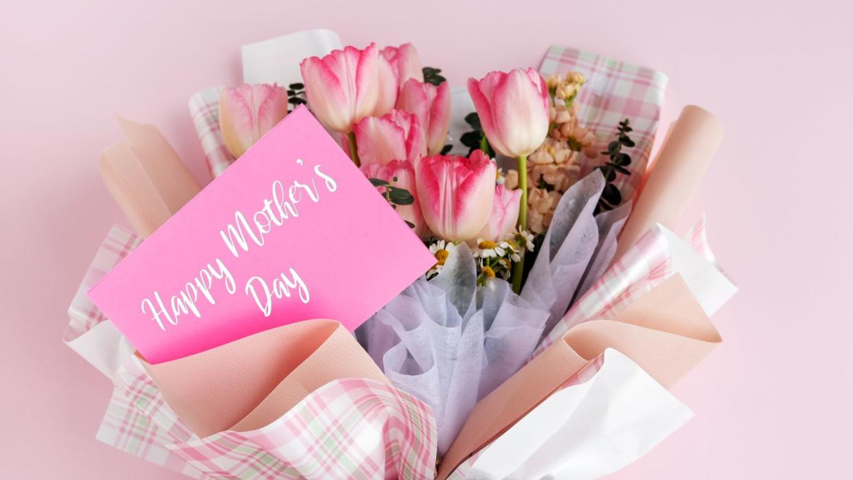 bouquet of pink tulips and other flowers wrapped in plaid paper with a pink card reading happy mothers day in white script