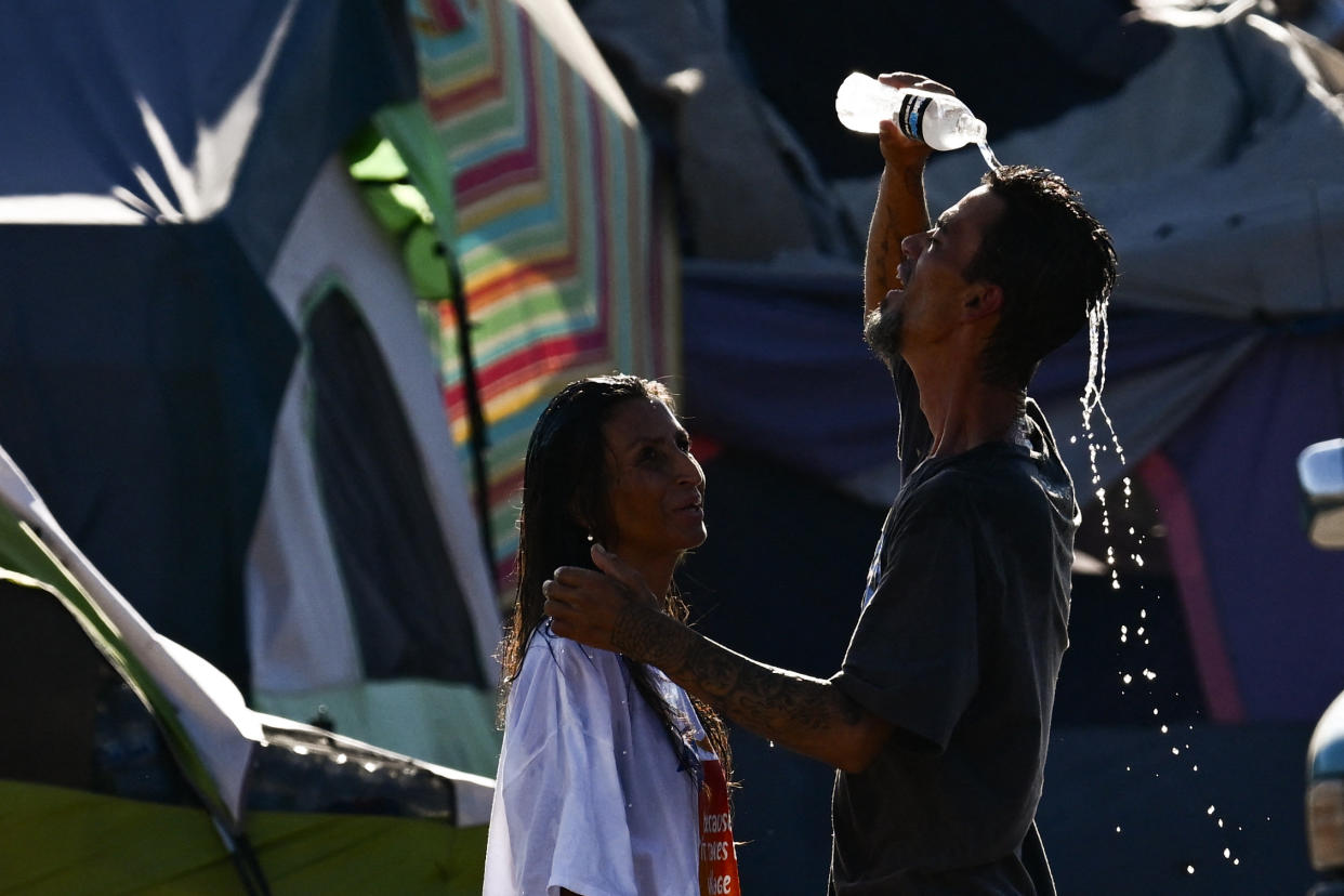 Two people pour water on themselves to cool off while residing in the Zone, a vast homeless encampment in Phoenix.