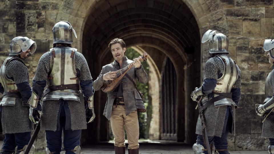 Chris Pine plays a lute near helmeted medieval soldiers