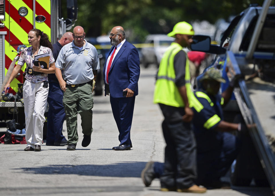 Police officers walk to the crime scene, Tuesday, July 9, 2019, in Cleveland. Police investigating the shooting death of a man in a vacant lot say they also found the bodies of a woman and two children in a nearby house. Authorities aren't saying how the three found inside the house Tuesday died, but they did say the four deaths are connected. (AP Photo/David Dermer)