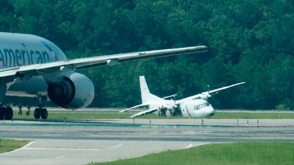 A twin-engine turbo prop aircraft sits on the grass near runway 5R-23L at Raleigh-Durham International Airport Saturday July 30, 2022. The plane made an emergency landing at RDU Friday after reporting landing gear issues.