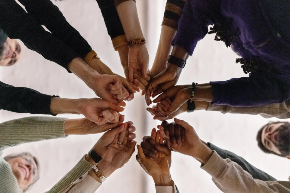 Low angle view of group of people in circle and holding their fists together during a group therapy session. People with fist put together during support group session.