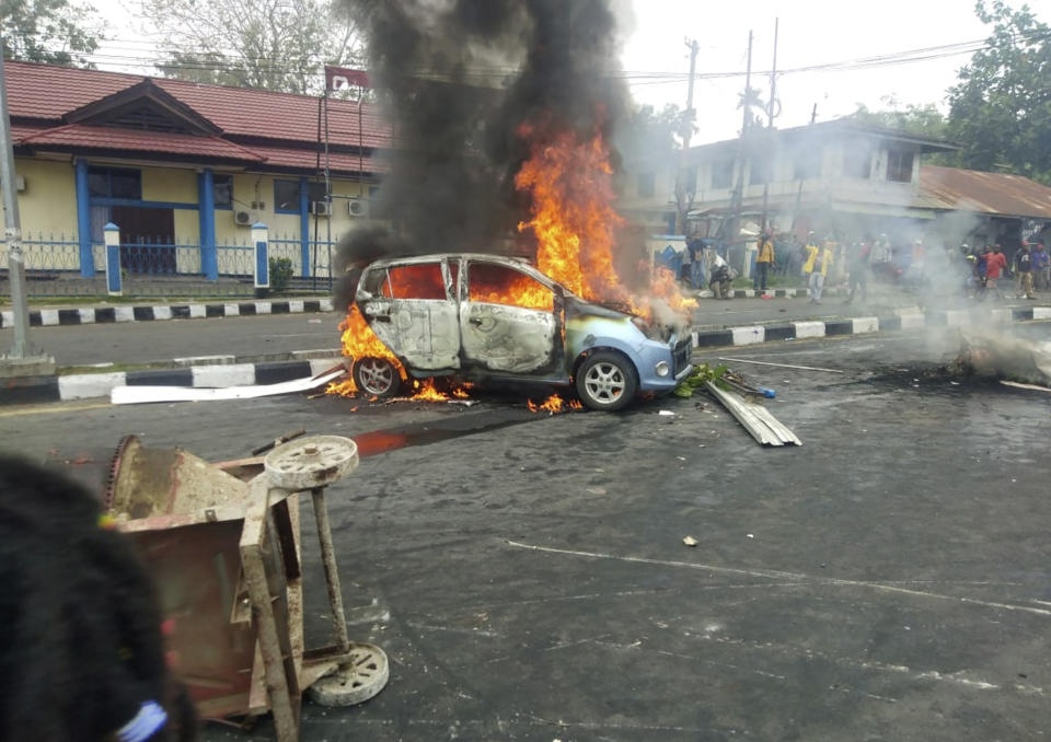 People look on as a car burns during a violent protest in Manokwari, Papua province, Indonesia, Monday, Aug. 19, 2019. The protest was sparked by accusations that Indonesian police who backed by the military, have arrested and insulted dozens of Papuan students in their dormitary in East Java's cities of Surabaya and Malang a day earlier. (AP Photo/Safwan Ashari Raharusun)