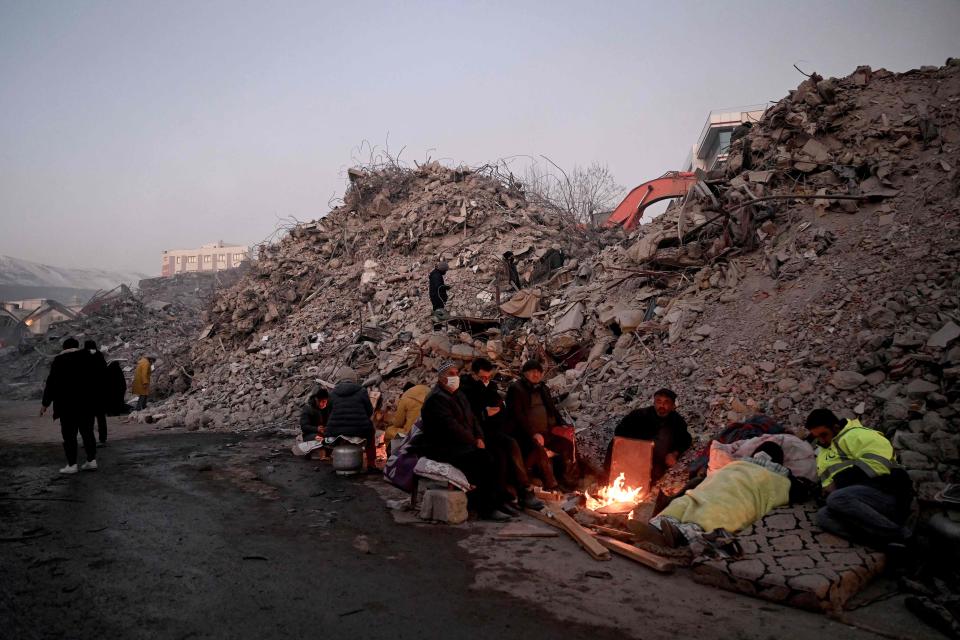 Relatives warm up around a fire in front of rubble of collapsed buildings as rescue teams continue to search victims and survivors, after a 7.8 magnitude earthquake struck the border region of Turkey and Syria earlier in the week, in Kahramanmaras on February 12, 2023.