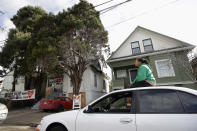 Sunday Simon, a supporter of homeless women who were occupying a house, sits on a car near the house, at left, in Oakland, Calif., Tuesday, Jan. 14, 2020. Homeless women ordered by a judge last week to leave a vacant house they occupied illegally in Oakland for two months have been evicted by sheriff's deputies. They removed two women and a male supporter Tuesday from the home before dawn in a case highlighting California's severe housing shortage and growing homeless population. (AP Photo/Jeff Chiu)