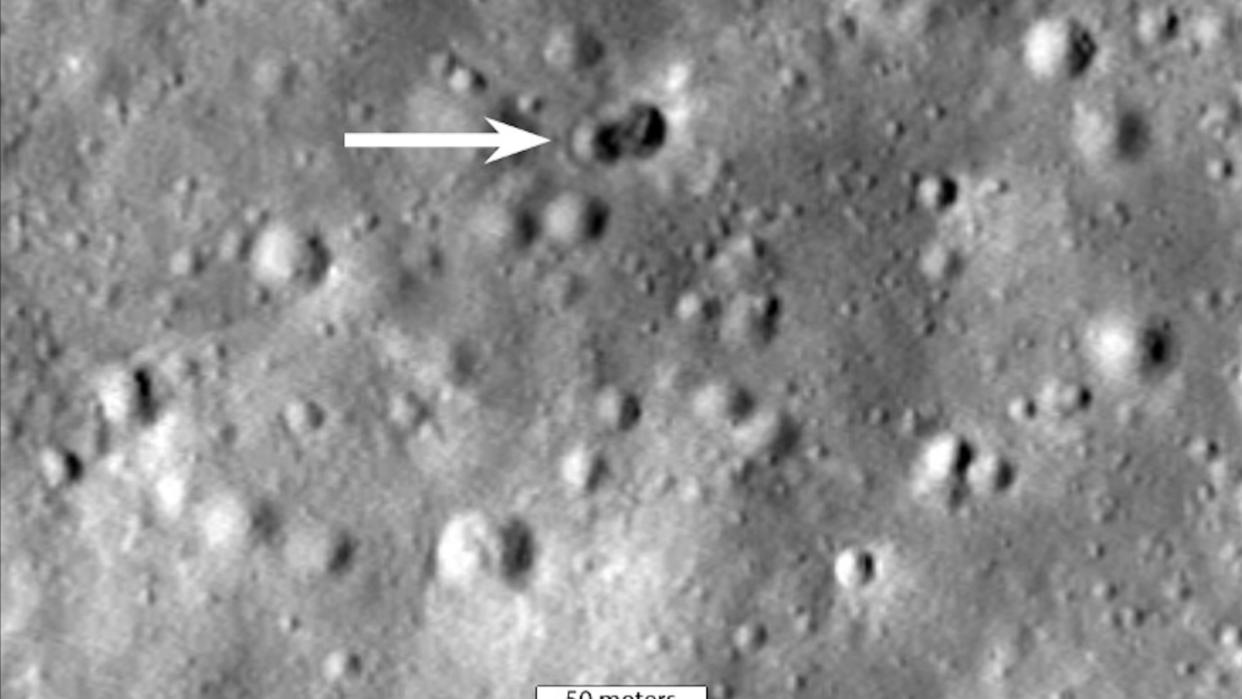  Black and white photo of the moon's surface, showing a fresh, dark double crater. 