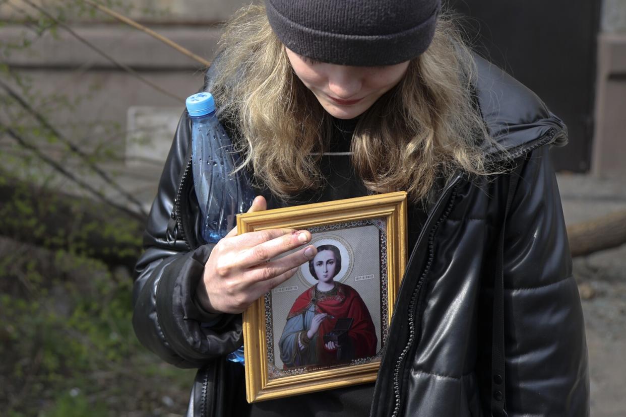 A woman holds a water bottle and a framed religious icon.