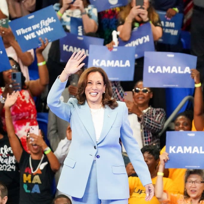 Kamala Harris waves to the crowd at a rally, surrounded by supporters holding 