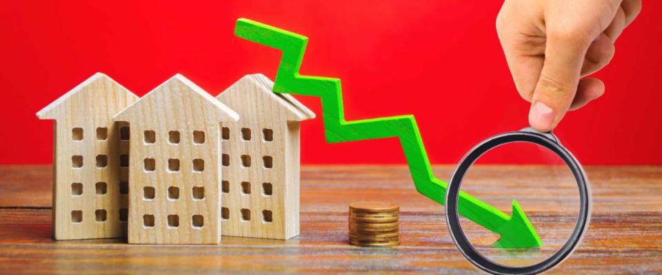 Miniature wooden houses and a green arrow down. The concept of falling mortgage rates