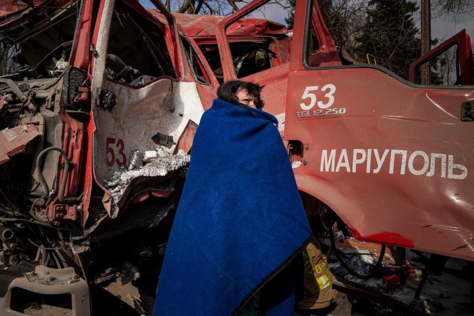 A woman covers herself with a blanket near a damaged fire truck after shelling in Mariupol (AP)