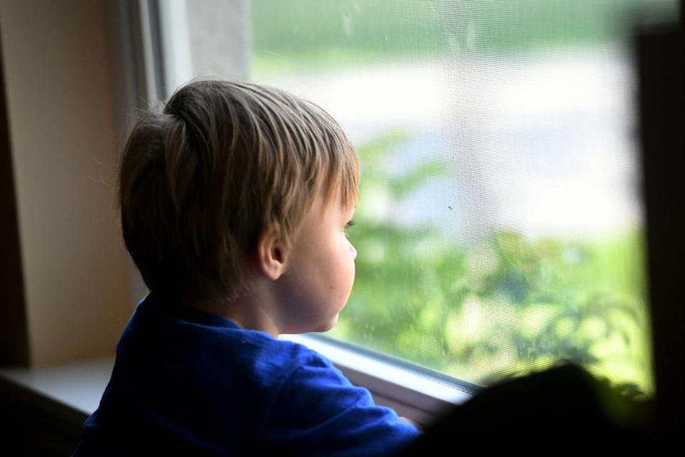 A young child, formerly in foster care, looks out the living room window. His parents fostered him since birth and ended up adopting him.