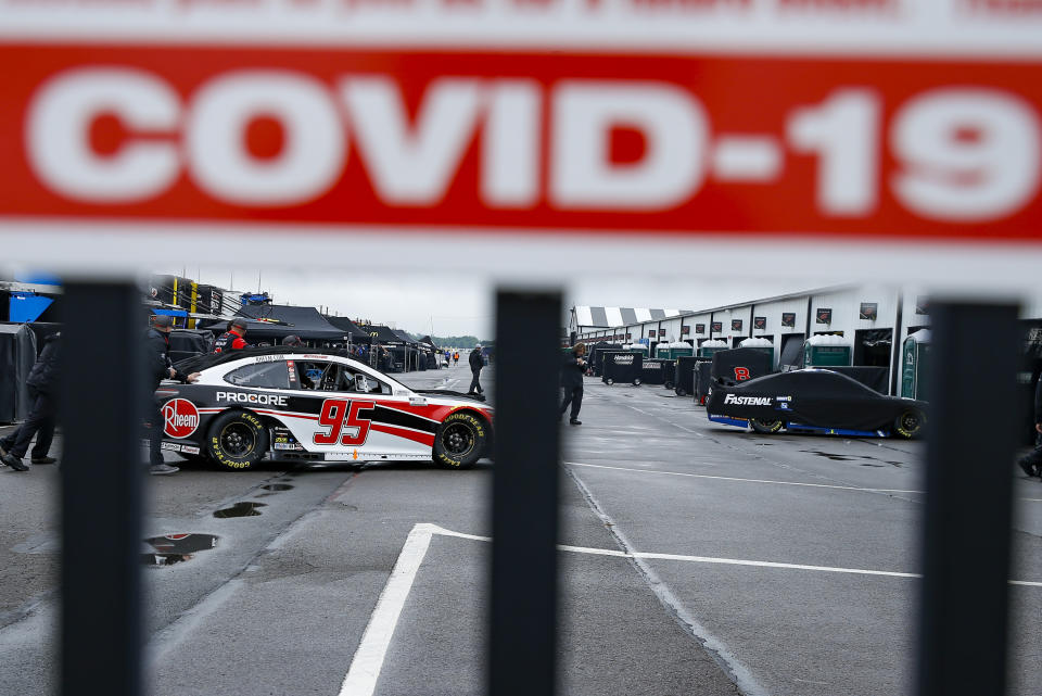 Crew members are visible under a COVID-19 alert sign as they push the car of Christopher Bell through the garage area in the morning before a scheduled NASCAR Cup Series auto race at Pocono Raceway, Saturday, June 27, 2020, in Long Pond, Pa. (AP Photo/Matt Slocum)