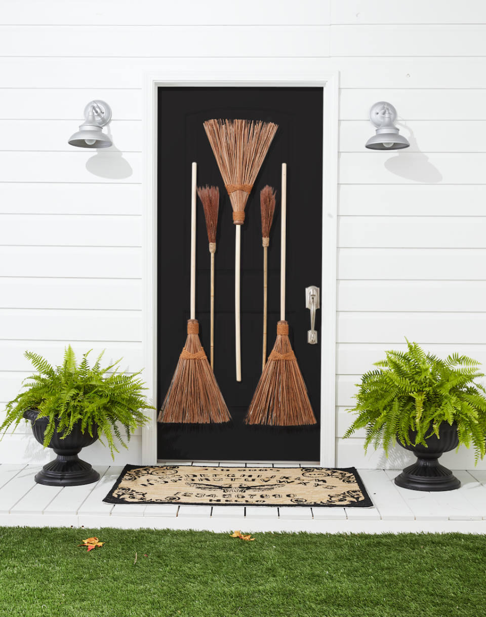 <p>If you're planning on wearing a <a href="https://www.countryliving.com/diy-crafts/g28304812/diy-witch-costume/" rel="nofollow noopener" target="_blank" data-ylk="slk:witch costume;elm:context_link;itc:0;sec:content-canvas" class="link ">witch costume</a> this year, why not decorate your door with broomsticks? Matching your costume to your decorations is always a good idea.</p><p><strong>Make the Broomstick Door:</strong> Drill a small hole in the handle of two large outdoor brooms. Hammer five small nails in front door. Hang two brooms, right sides up, through holes. Hang a third large broom and two small "witches brooms" by threading the bristles over the remaining three nails. Add black plastic Grecian urn planters and "Spirit Board" doormat. </p>