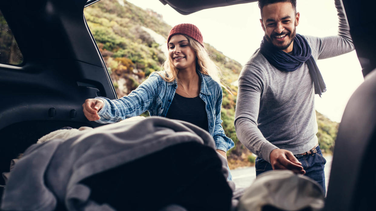 Happy couple on a vacations, taking their luggage out of car boot.