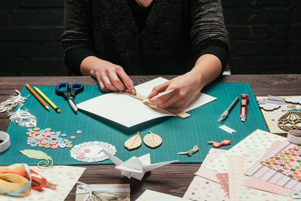 A person sitting at a table with scissors, pencils, paper, and various other crafting items.