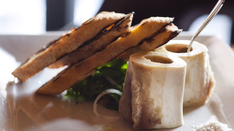 bone marrow with toast and salad on white plate