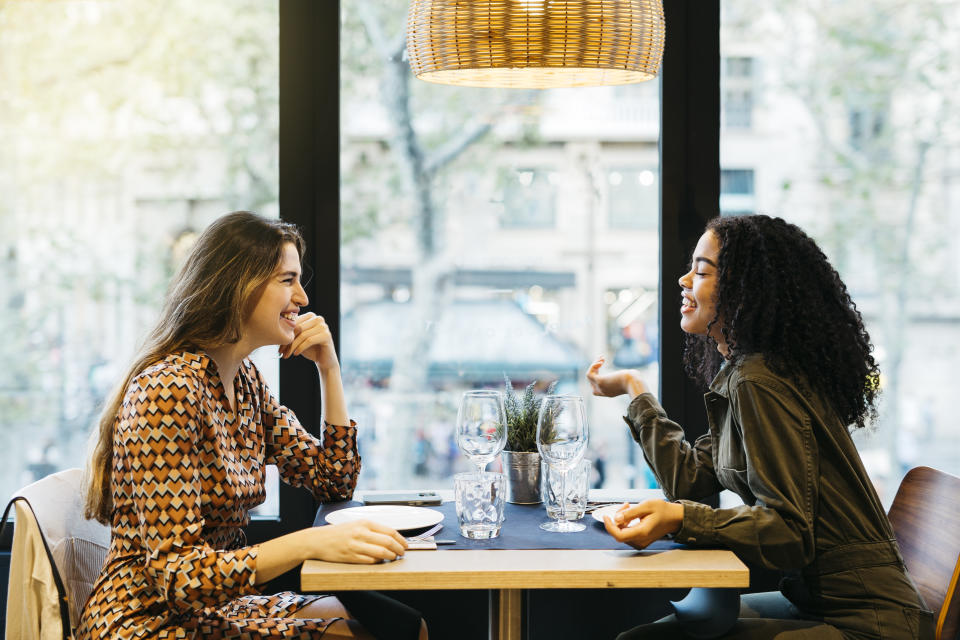 Two young smiling women sitting on a restaurant table