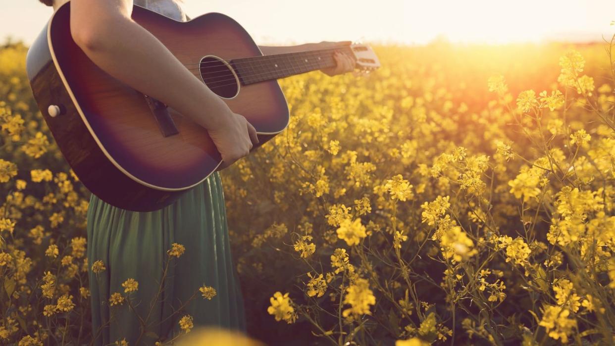 woman holding a guitar in a field of yellow flowers who might be singing easter songs