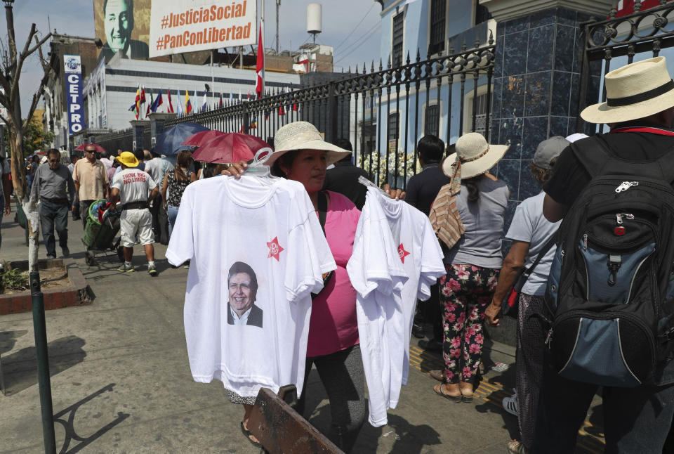 A woman sells T-shirts featuring Peru's late President Alan Garcia outside his political party's headquarters where his wake takes place in Lima, Peru, Thursday, April 18, 2019. Garcia shot himself in the head and died Wednesday as officers waited to arrest him in a massive graft probe that has put the country's most prominent politicians behind bars and provoked a reckoning over corruption. (AP Photo/Martin Mejia)