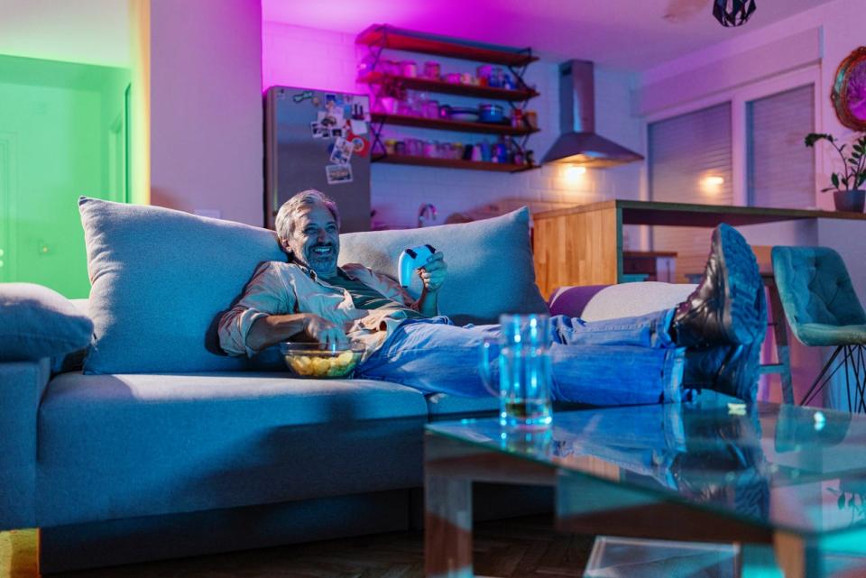 Mature man playing video games at home, his home interior lit with multicolored lights.