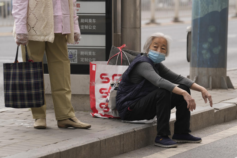 An elderly woman wearing mask waits at a bus-stop in Chaoyang District on Monday, April 25, 2022, in Beijing. (AP Photo/Ng Han Guan)