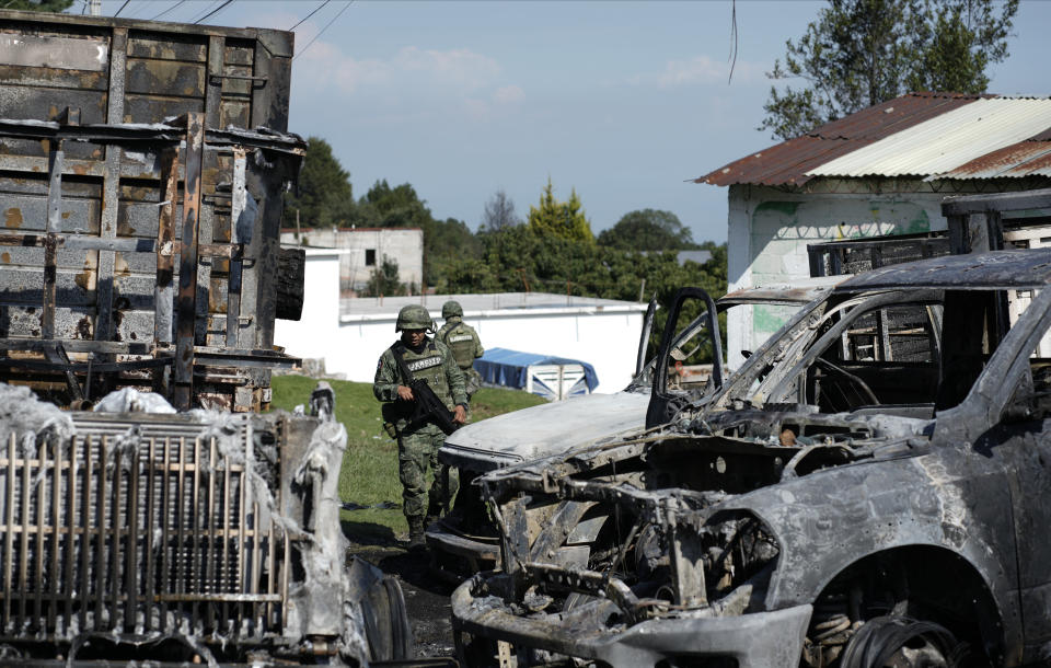 Mexican Army soldiers walk around the burnt-out remains of several trucks that were torched during a protest against a raid targeting illegal logging and sawmills in the pine forests outside of Huitzilac, Mexico, Wednesday, Aug. 2, 2023. Morelos state prosecutors said the raid involved at least 300 officers of the state police, the National Guard and the army. (AP Photo/Eduardo Verdugo)