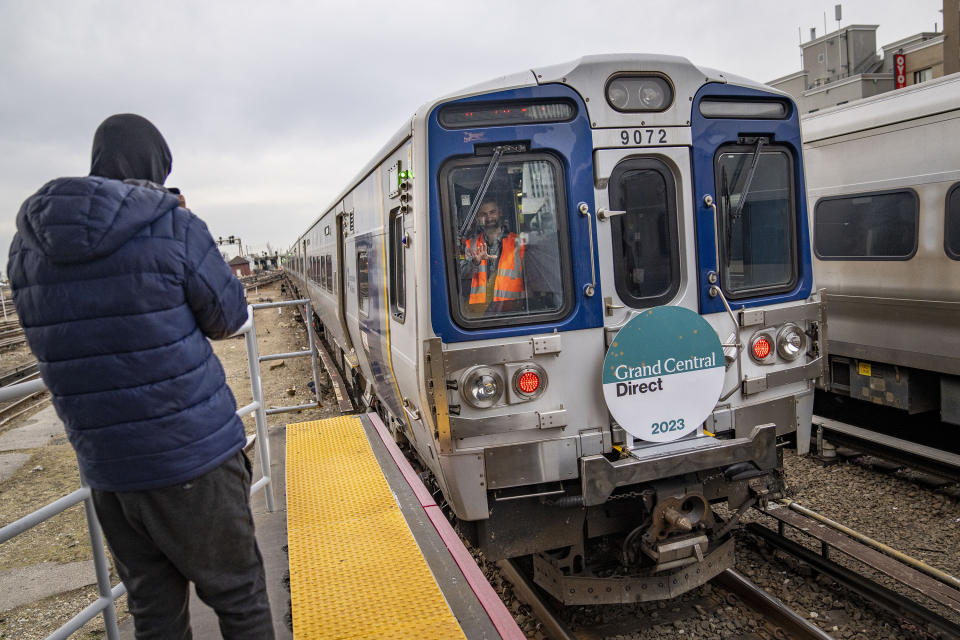 A rider in the rear conductor's booth waves to photographers on the platform after their Long Island Rail Road train departs for its inaugural trip from Jamaica station towards Grand Central Terminal, Wednesday, Jan. 25, 2023, in the Queens borough of New York. After years of delays and massive cost overruns, the railway project has begun shuttling its first passengers between Long Island to the latest addition to New York City's iconic Grand Central Terminal, dubbed Grand Central Madison because of its location along Madison Avenue.(AP Photo/John Minchillo)