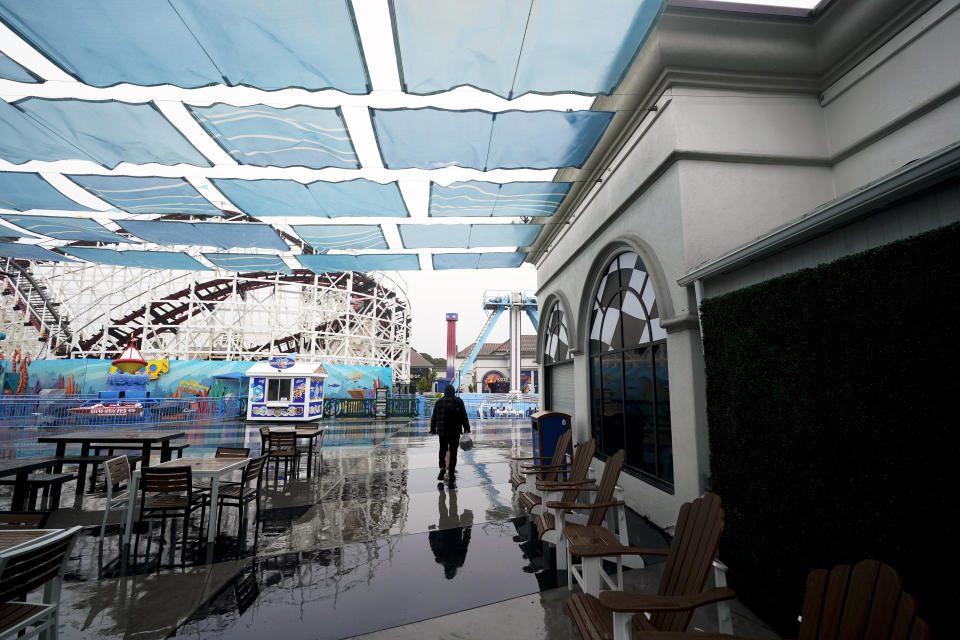 A worker walks among a vacant Belmont Park as rain engulfs the area, Tuesday, March 21, 2023, in San Diego. Californians are tired. Tired of the rain, tired of the snow, tired of stormy weather and the cold, relentlessly gray skies that have clouded the Golden State nearly nonstop since late December. (AP Photo/Gregory Bull)