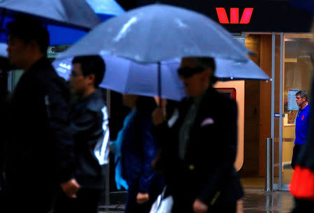 FILE PHOTO: Pedestrians hold umbrellas as they walk past a branch of the Westpac Banking Corp in central Sydney, Australia, March 30, 2017. REUTERS/David Gray/File Photo