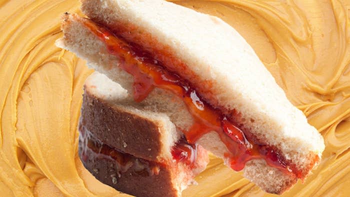 Peanut butter and jelly sandwich with a bite taken out, on a peanut butter-covered surface