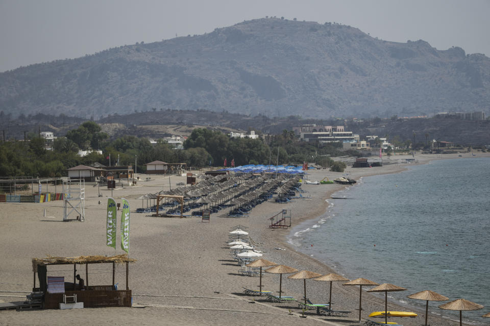 FILE - Abandoned sun beds and umbrellas stand at the beach as a burnt hill is seen in the background after a wildfire, in Kiotari village, on the Aegean Sea island of Rhodes, southeastern Greece, on Thursday, July 27, 2023. Tourists at a seaside hotel on the Greek island of Rhodes snatched up pails of pool water and damp towels as flames approached, rushing to help staffers and locals extinguish one of the wildfires threatening Mediterranean locales during recent heat waves. (AP Photo/Petros Giannakouris, File)