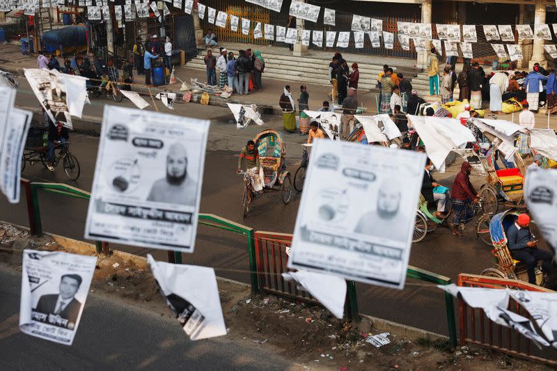 Commuters pass by as posters of different election candidates hang on the street ahead of the general election in Dhaka