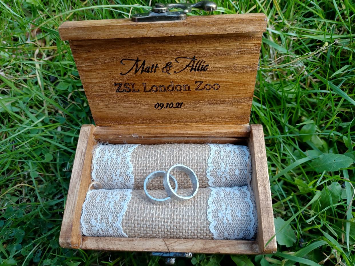 Two silver rings sit within a light brown wooden box on a green background