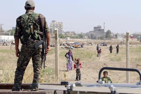 A Kurdish People's Protection Units (YPG) fighter looks at makeshift tents between the Syrian and Turkish borders of residents who fled Maskana town in the Aleppo countryside, as he stands in Tel Abyad town, Raqqa governorate, Syria, June 23, 2015. REUTERS/Rodi Said