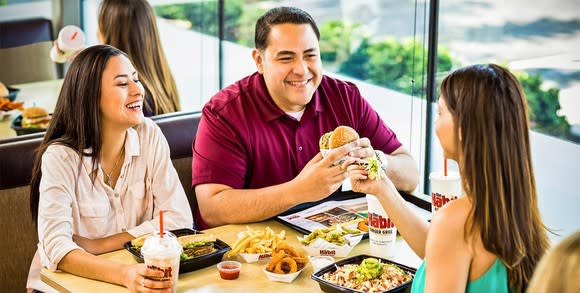 A group of three people sitting beside a window eating burgers and a salad at The Habit.